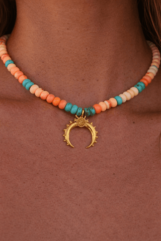 Close-up of opal beaded necklace with turquoise accents and gold crescent pendant worn on skin
