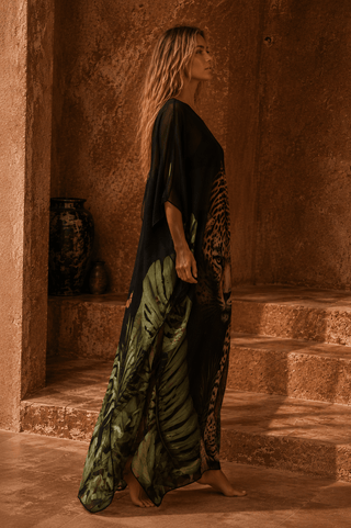 Woman in a long, dark green dress with a patterned edge standing in a sunlit stone alcove.