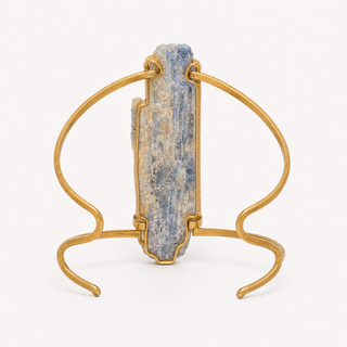 A gold-toned metal wire stand holding a vertical blue-gray stone or crystal, photographed against a clean white background.