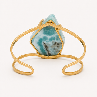 A gold wire cuff bracelet featuring a large, faceted natural Larimar stone with its characteristic turquoise and white marbling, set in a polished gold bezel.