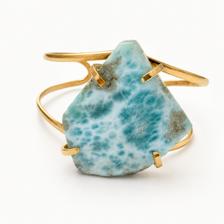 A gold wrap cuff bracelet featuring a large, irregular-shaped natural larimar stone with a textured turquoise-blue and white pattern, displayed on a clean white background.