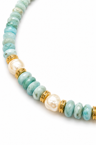 A close-up of a beaded necklace featuring light blue marbled beads, white baroque pearls, and gold spacers on a white background.