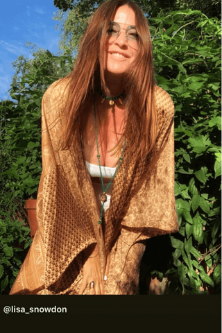 Person wearing a brown quilted jacket sitting outdoors with greenery in the background