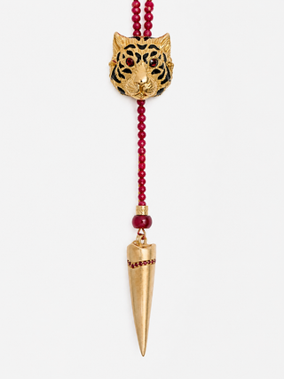 A gold-toned tiger head pendant necklace with black enamel details, hanging from a red beaded cord with a gold cone-shaped pendant below, shown against a light gray background.