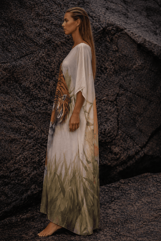 Woman wearing a long, flowing dress with artistic design against a textured wall.