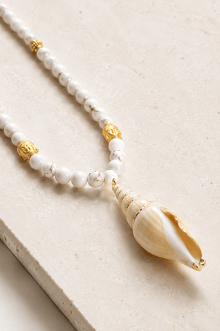 Necklace with white beads and a shell pendant on a beige background